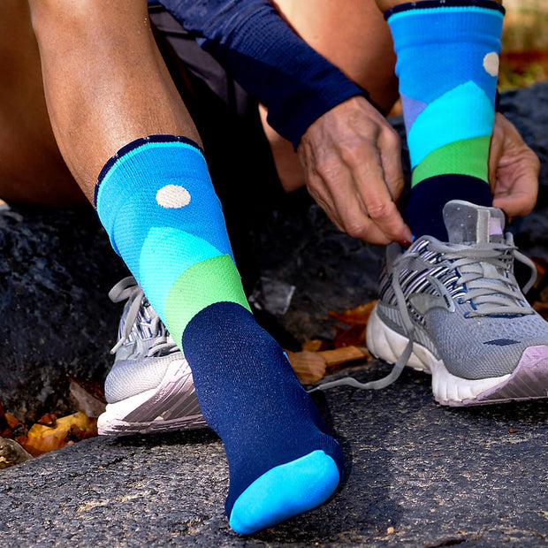 Close-up of runner putting shoe on over blue compression crew socks with moonlit mountains design