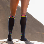 Close-up of athlete legs wearing slate compression socks with vertical multi-colored XXXX at ankles