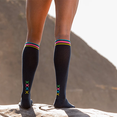 Close-up of athlete legs wearing slate compression socks with vertical multi-colored XXXX at ankles