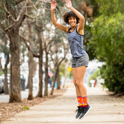 Happy woman jumping with arms in the air wearing orange compression crew socks featuring moonlit mountains design
