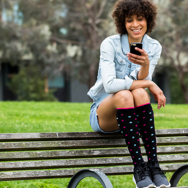 Woman on park bench wearing black compression socks with pink and light blue dots