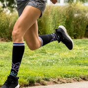 Close-up of runner's legs wearing black compression socks with lotus flowers and light blue & purple accents