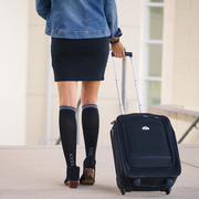 Traveler with suitcase wearing black compression socks with grey stripe at top and vertical grey XXXX on ankles