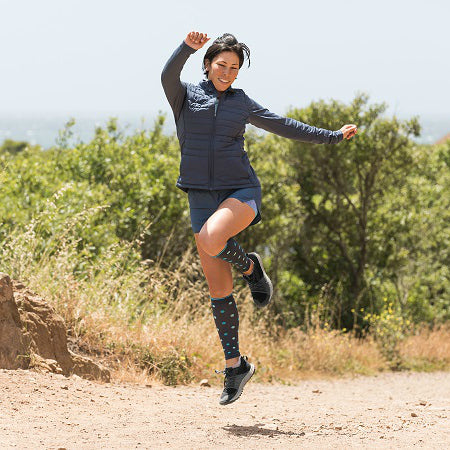 Runner doing a skip wearing slate polka-dotted compression calf sleeves