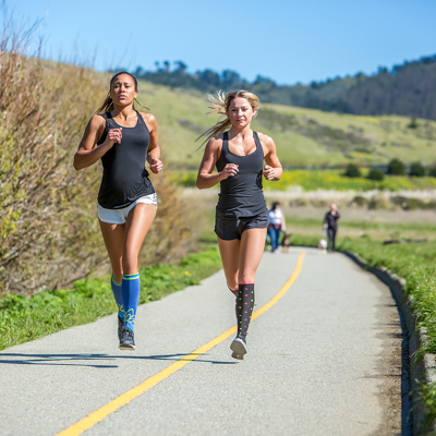 Woman running with friend & wearing black compression socks with pink and light blue dots